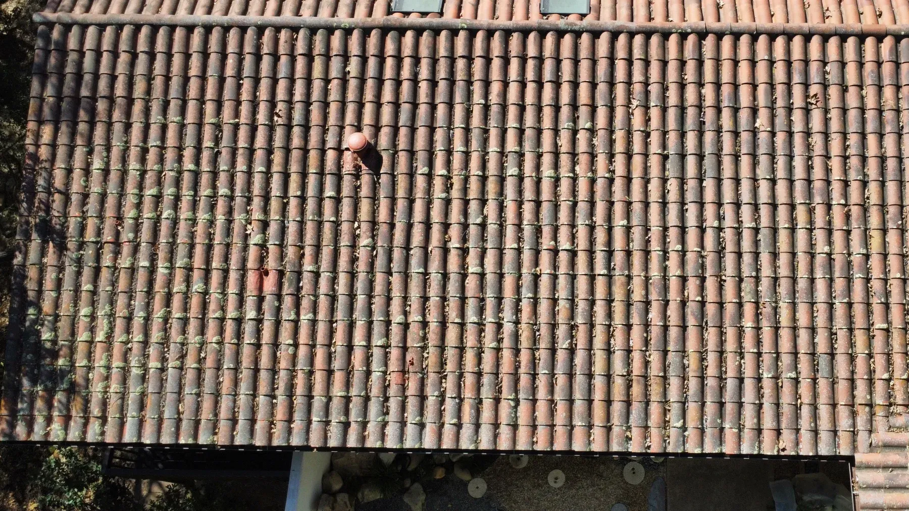 Close drone view of clay roof tiles covered in moss and lichen before cleaning